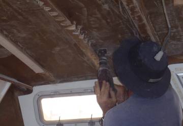 Jon, covered in sweat, drilling cores under the port sail-track