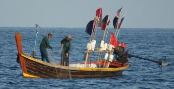 Thai fishermen pull a net. Note flags with floats.